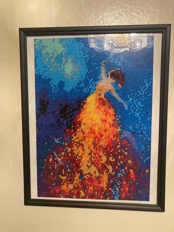 Inramad diamond painting med motiv av en kvinna i glittrande klänning mot blå bakgrund.